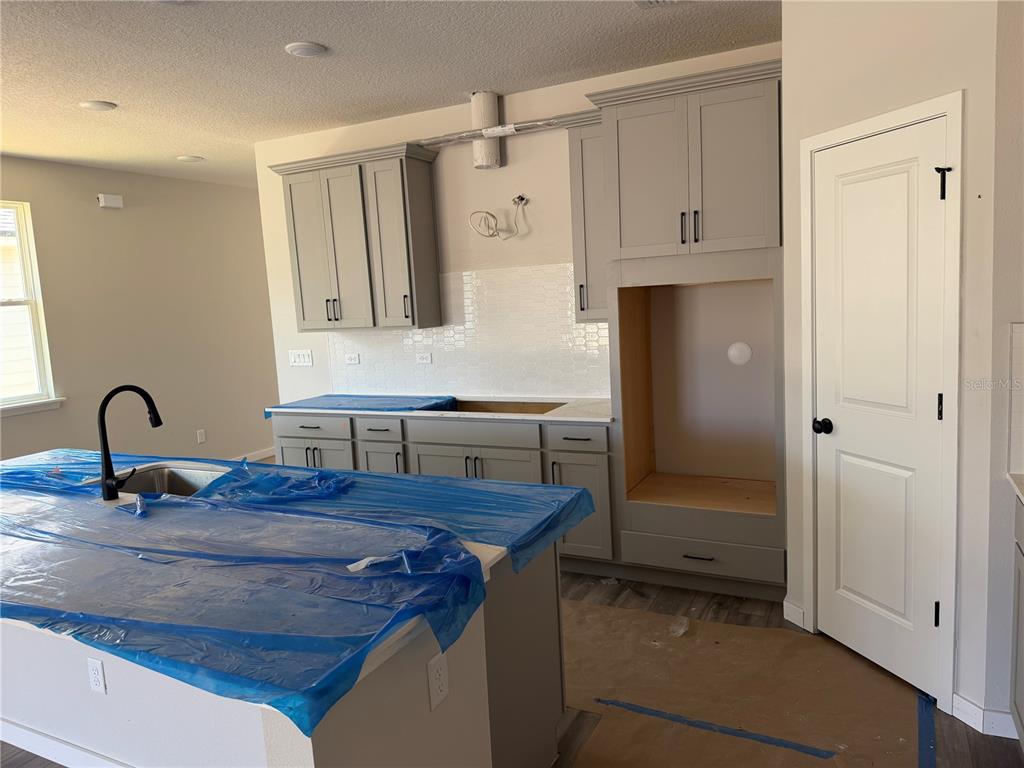 A kitchen under construction features gray cabinets, a center island, and a tiled backsplash — 28 PERSEUS AVENUE, FLAGLER BEACH, FL