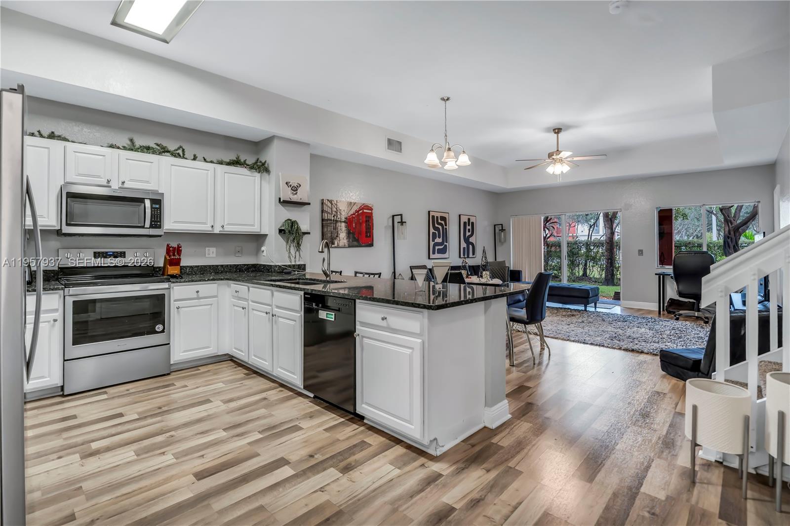 A kitchen features white cabinets, dark granite countertops, a breakfast bar, and wood-look flooring — 7401 Palomino Dr # 1, Davie FL 33024, DAVIE, FL