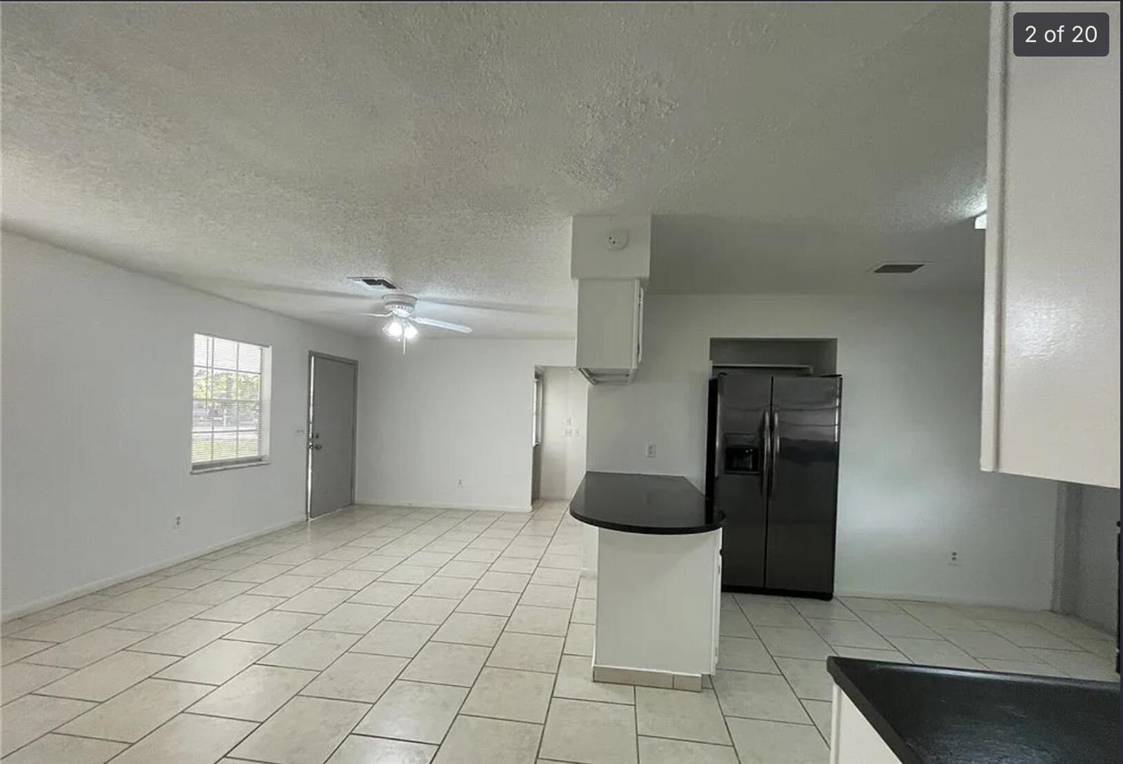 An open-concept kitchen and living area features white walls, light tile flooring, and a peninsula — 2385 88th Avenue, Vero Beach FL 32966, VERO BEACH, FL