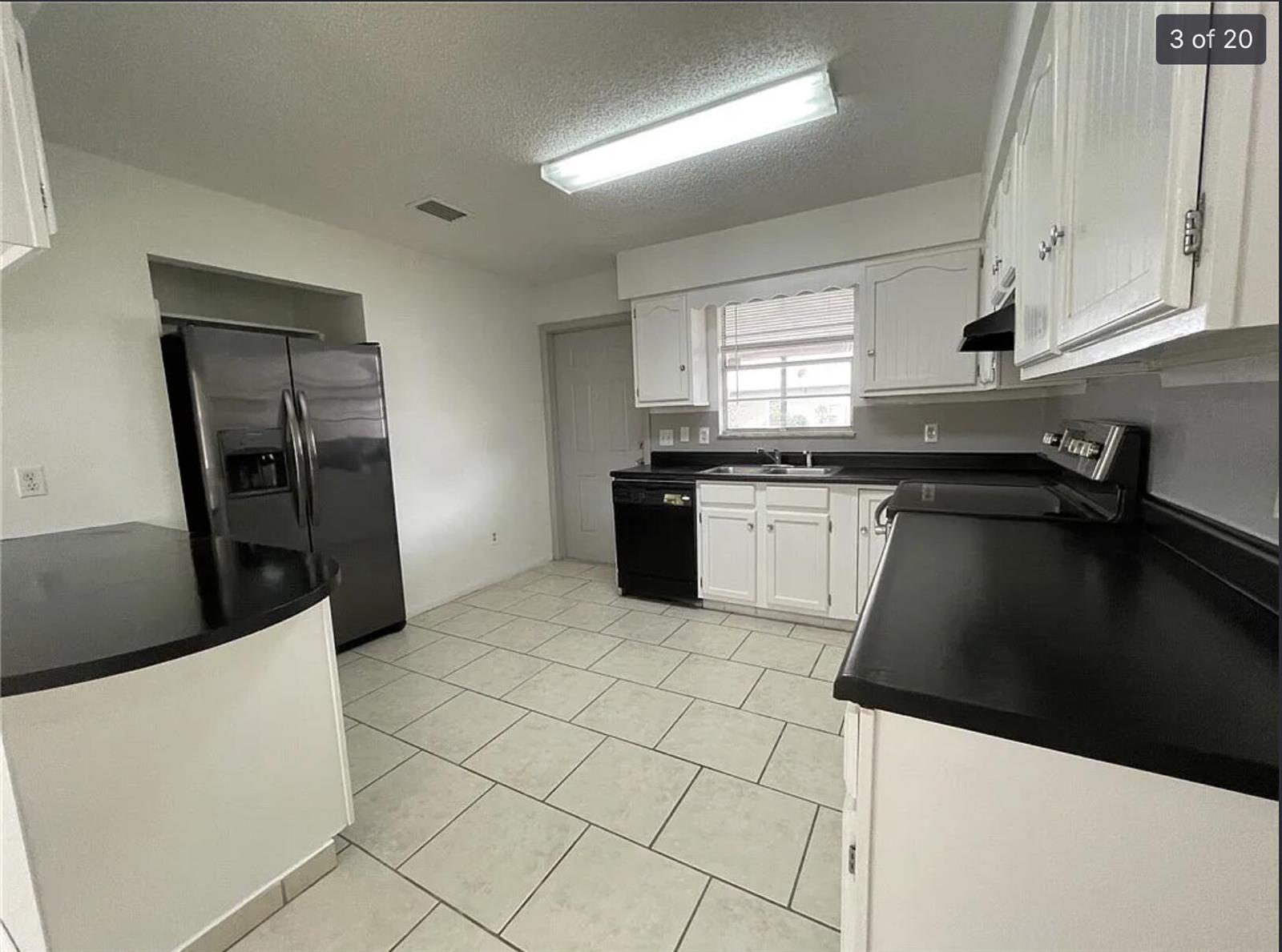 A kitchen features white cabinets, black countertops, stainless steel appliances, and light-colored tile flooring — 2385 88th Avenue, Vero Beach FL 32966, VERO BEACH, FL
