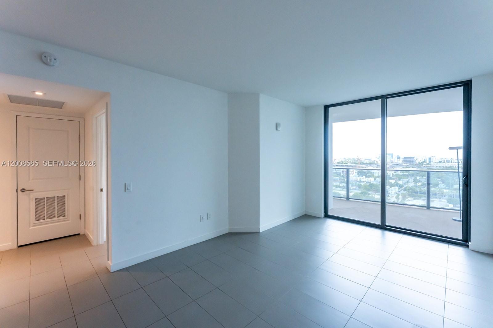An empty room features gray tile flooring, white walls, and a sliding glass door to a balcony — 1600 NE 1st Ave # 1814, Miami FL 33132, MIAMI, FL
