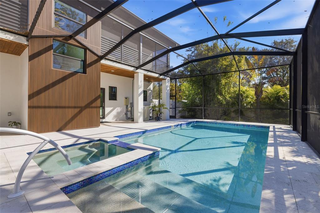 A swimming pool and spa are enclosed by a screen cage next to a modern home — 639 43RD AVENUE N, ST PETERSBURG, FL