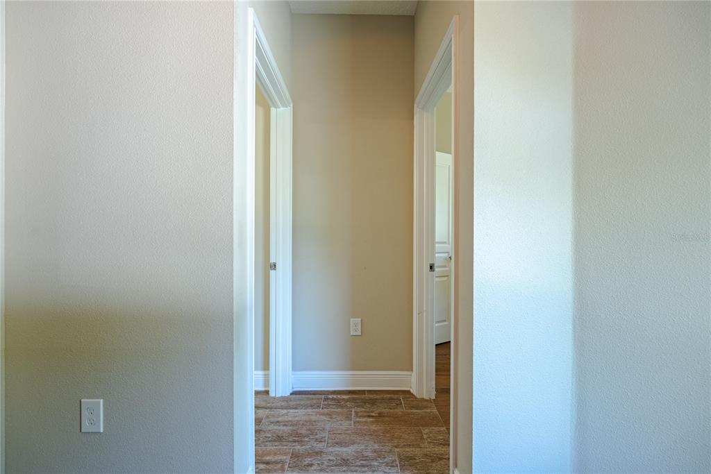 A hallway with tile flooring leads to two doorways and a beige wall with an outlet — 1908 W NASSAU STREET, TAMPA, FL