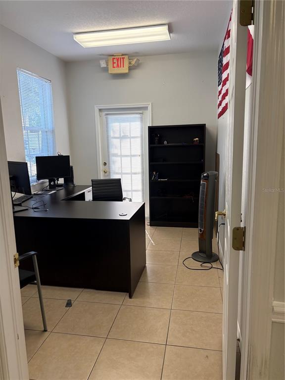 An office features a dark L-shaped desk, a black bookshelf, a tower fan, and tile flooring — 12187-12189 W LINEBAUGH AVENUE, TAMPA, FL
