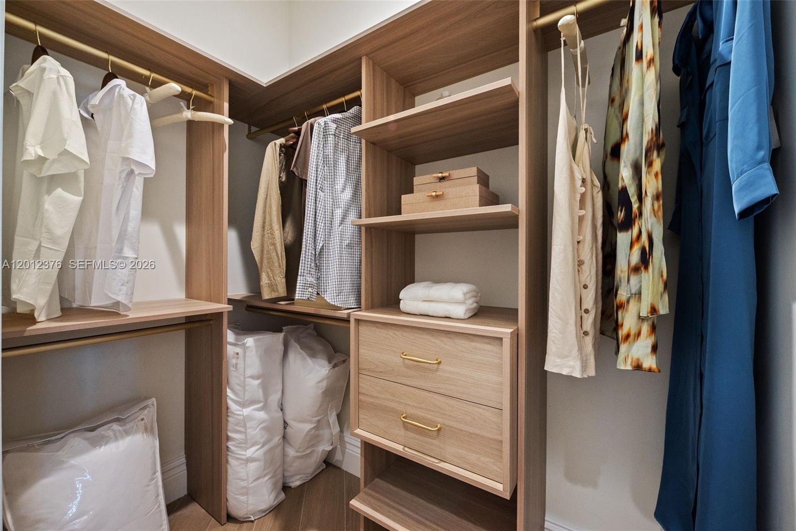 A walk-in closet features light wood shelving, hanging rods, and built-in drawers with gold hardware — 2700 NW 2nd ave # 708, Miami FL 33127, MIAMI, FL
