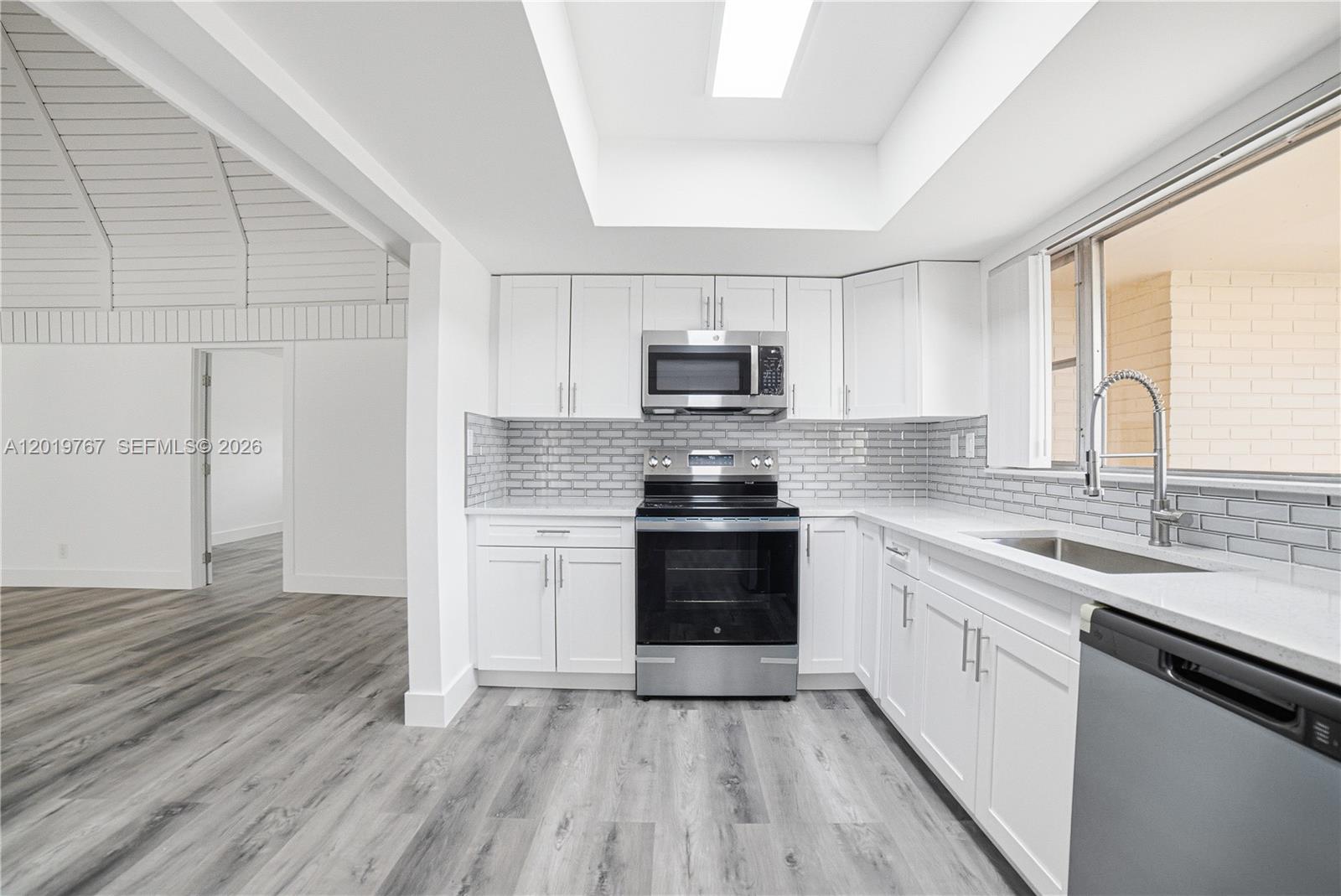 A kitchen features white cabinets, stainless steel appliances, gray subway tile, and wood-look flooring — 5201 Yellow Pine Ln # 0, Tamarac FL 33319, TAMARAC, FL