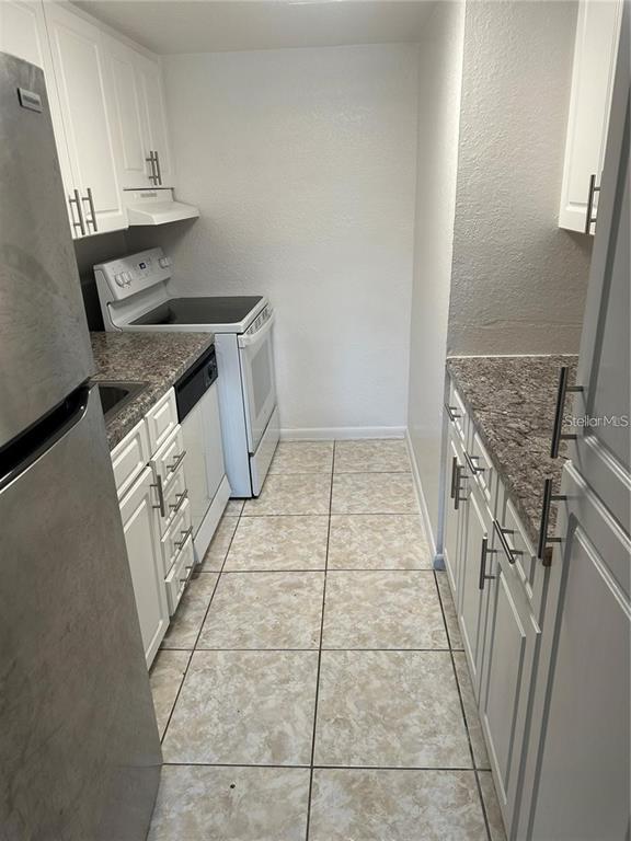 A galley-style kitchen features white cabinets, granite-look countertops, and light-colored tile flooring — 778 RIDENHOUR CIRCLE UNIT 778, ORLANDO, FL