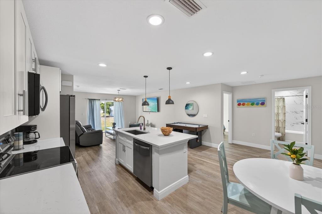 An open-concept kitchen with a white island and stainless steel appliances overlooks a living area — 12114 CLARENDON AVENUE, PORT CHARLOTTE, FL