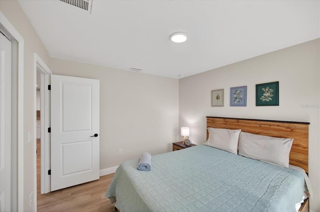 A bedroom features a bed with a wooden headboard, light flooring, and three framed pictures — 12114 CLARENDON AVENUE, PORT CHARLOTTE, FL