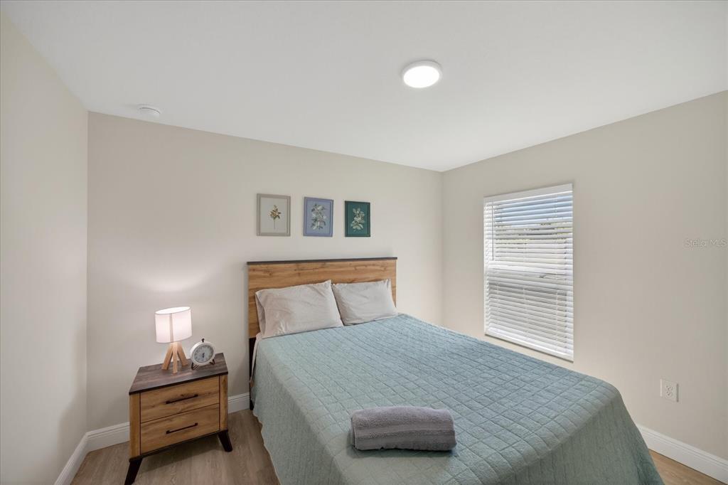 A bedroom features a bed with a teal quilt, a wooden nightstand, and a window — 12114 CLARENDON AVENUE, PORT CHARLOTTE, FL