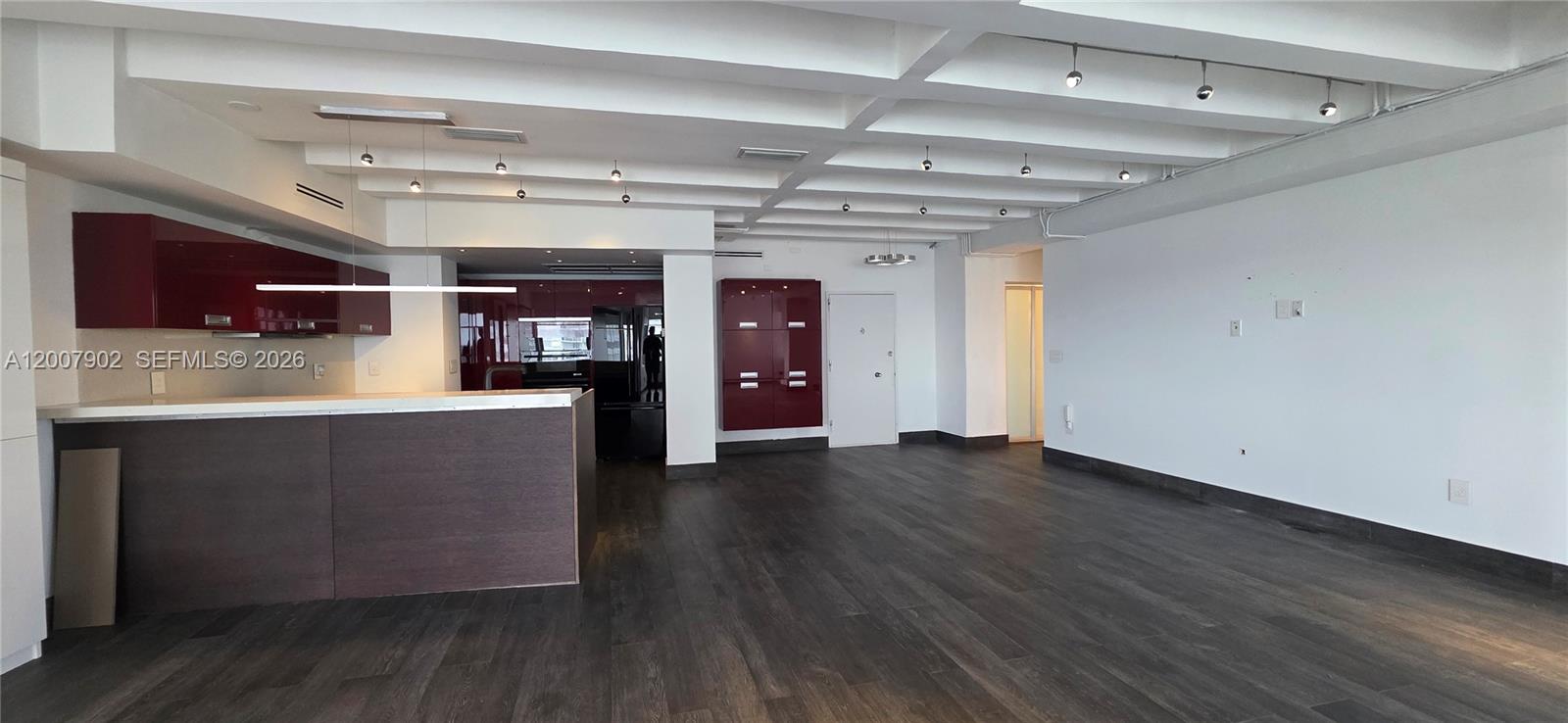 An open-concept living area features dark wood flooring, white beamed ceilings, and red kitchen cabinetry — 5255 Collins Ave # 7G, Miami Beach FL 33140, MIAMI BEACH, FL
