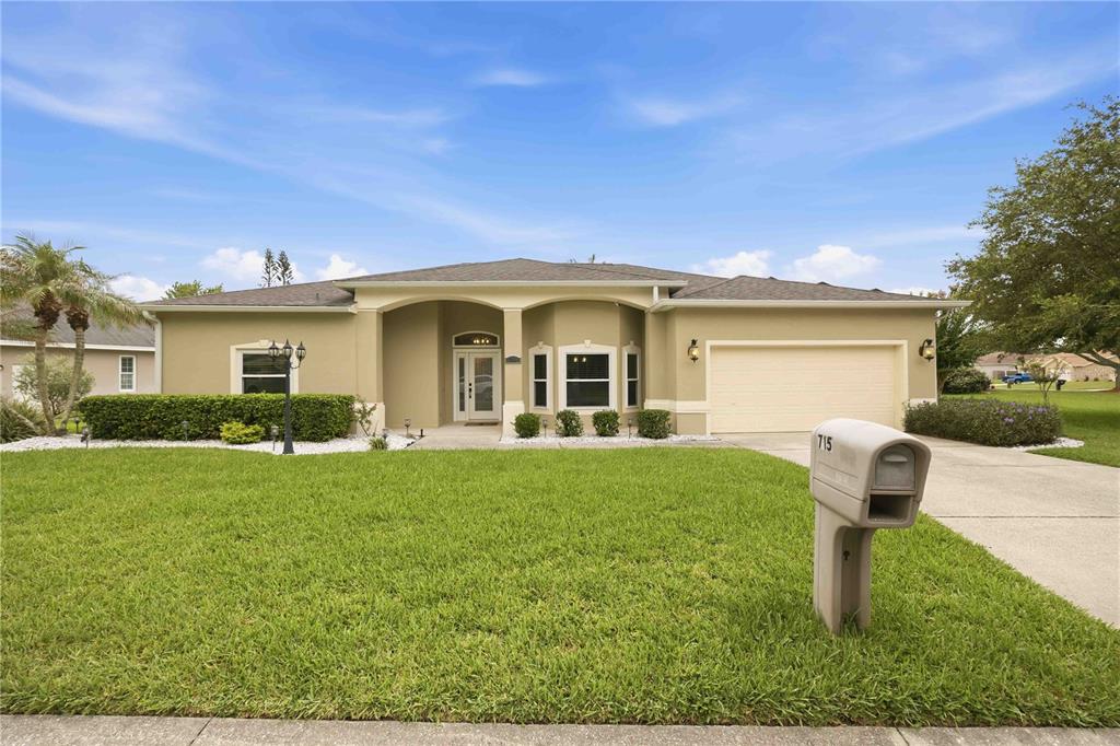 A single-story suburban house with a tan stucco exterior, a two-car garage, and a lawn — 715 JESSANDA CIRCLE, LAKELAND, FL
