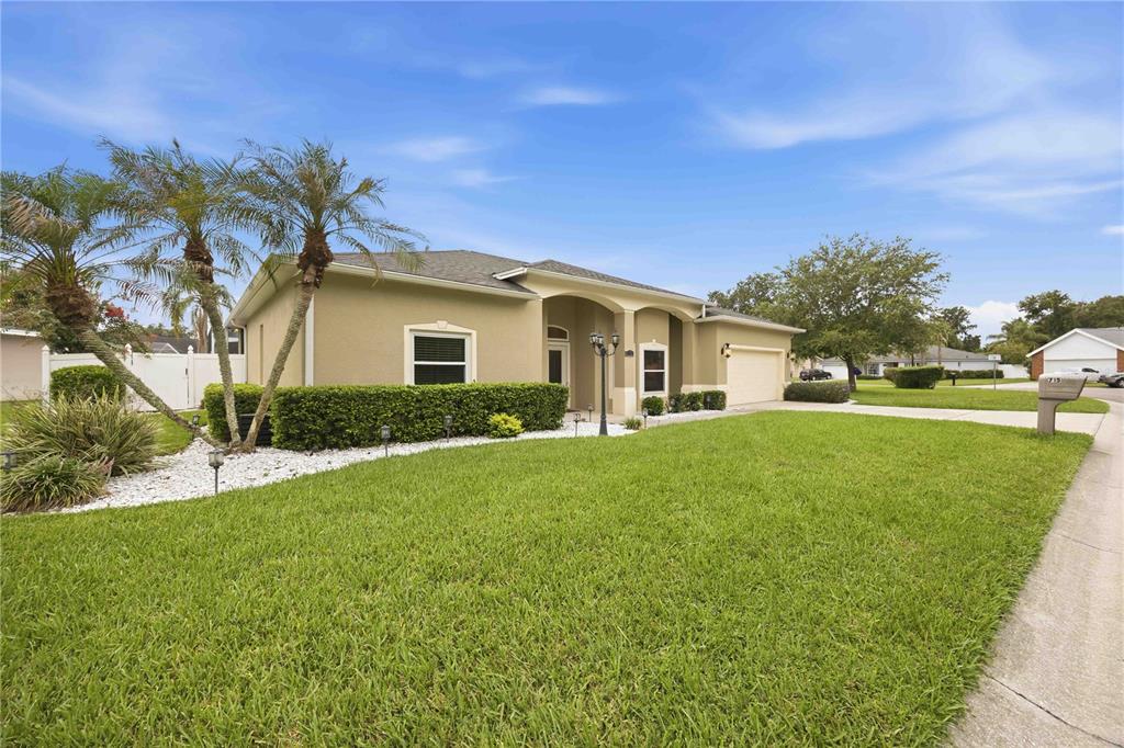 A single-story tan house with a two-car garage, palm trees, and a manicured lawn — 715 JESSANDA CIRCLE, LAKELAND, FL