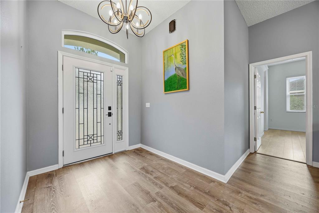An entryway with light gray walls, wood-look flooring, a glass-paneled front door, and a chandelier — 715 JESSANDA CIRCLE, LAKELAND, FL
