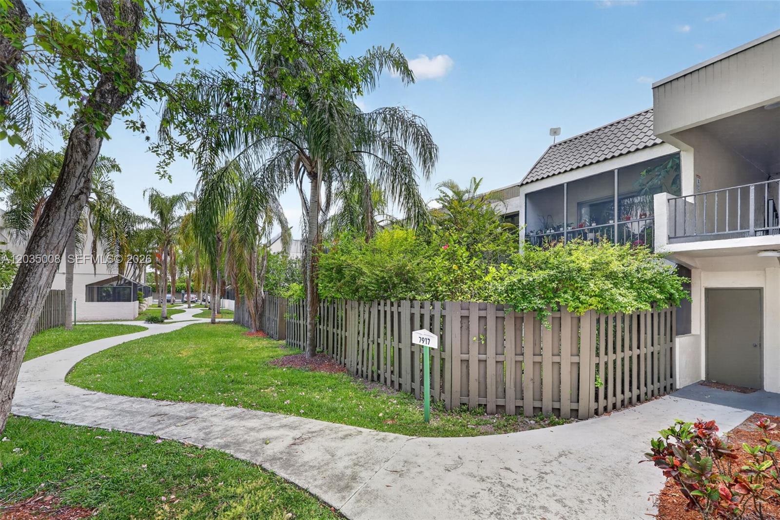 A sidewalk winds past a fenced patio and a two-story building with a screened balcony — 7917 SW 104th St # 201F, Miami FL 33156, MIAMI, FL