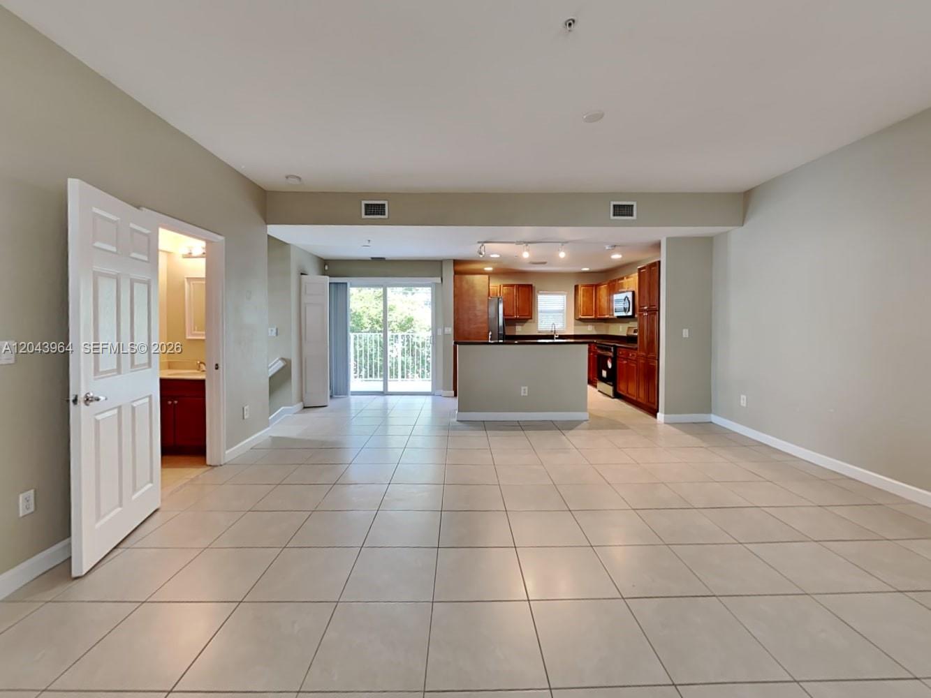 An open-concept living area features tile flooring, a kitchen with wood cabinets, and a balcony — POMPANO BEACH, FL