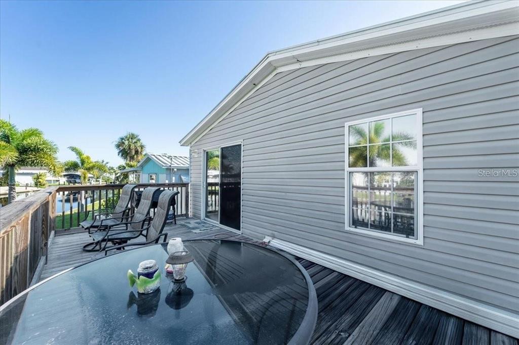 A wooden deck with patio furniture sits outside a house with light gray vinyl siding — 3127 BAYSIDE PARKWAY, PUNTA GORDA, FL