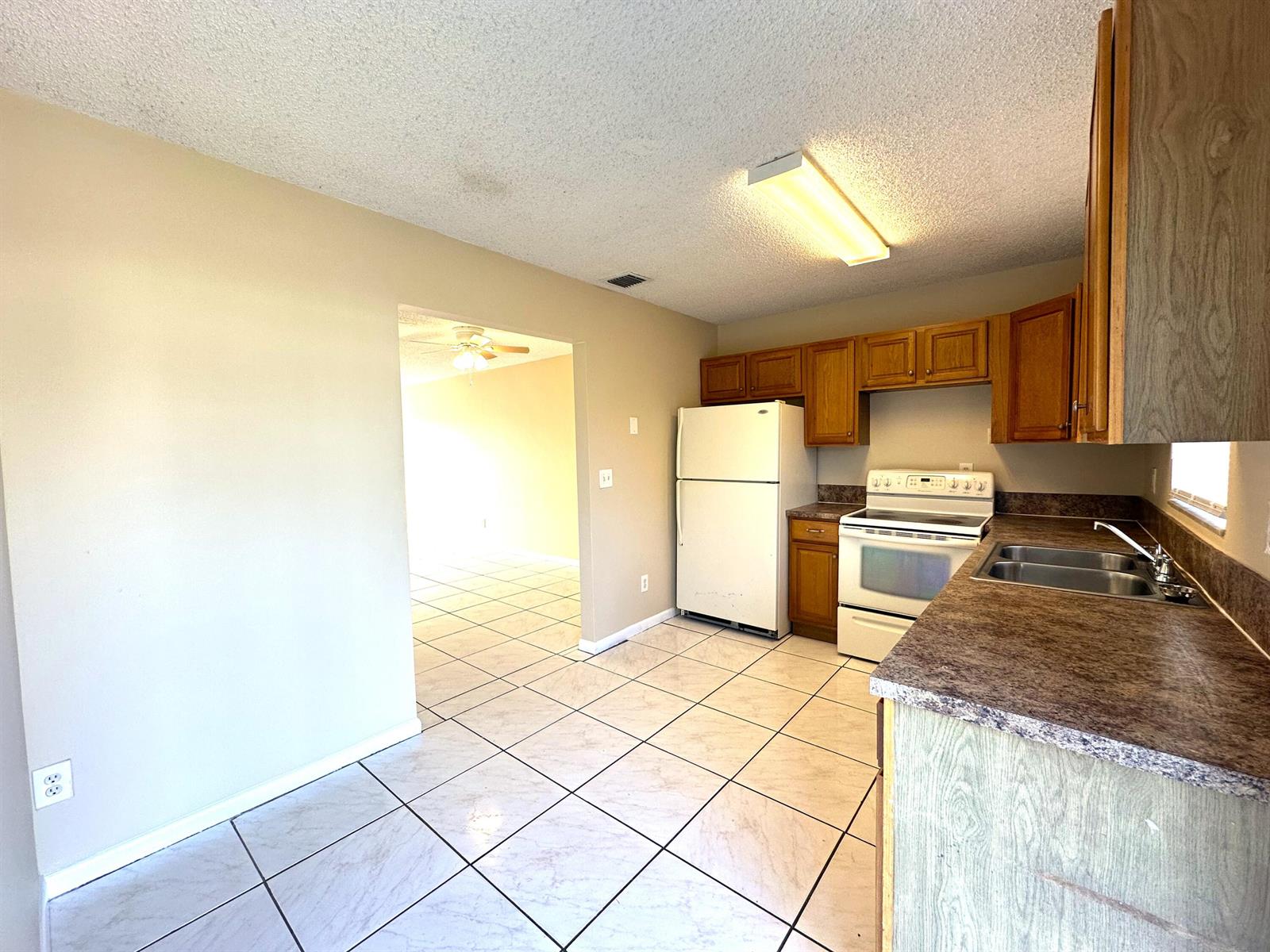 A kitchen with white appliances, wood cabinets, brown countertops, and light-colored tile flooring — 3365 SE Garden Street # 3365, Stuart FL 34997, STUART, FL
