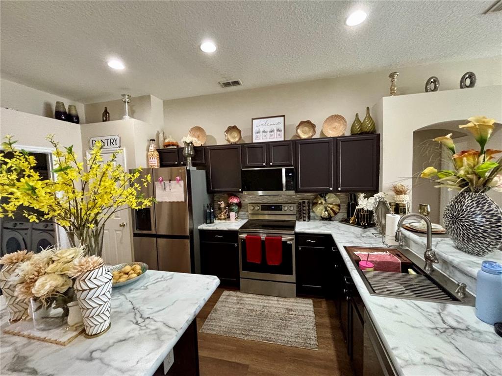 A kitchen features dark cabinets, marble-patterned countertops, stainless steel appliances, and a central island — 2146 BLACKSTONE LANDING DRIVE, KISSIMMEE, FL