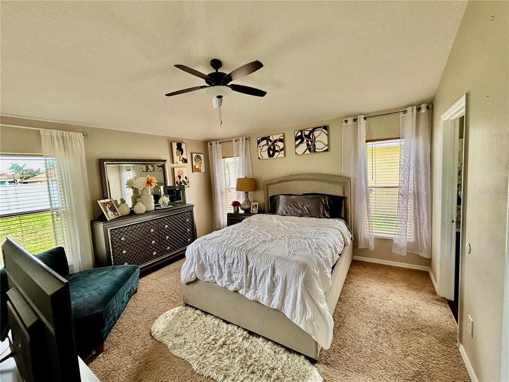 A bedroom features a bed with white bedding, a dresser, a ceiling fan, and windows — 2146 BLACKSTONE LANDING DRIVE, KISSIMMEE, FL
