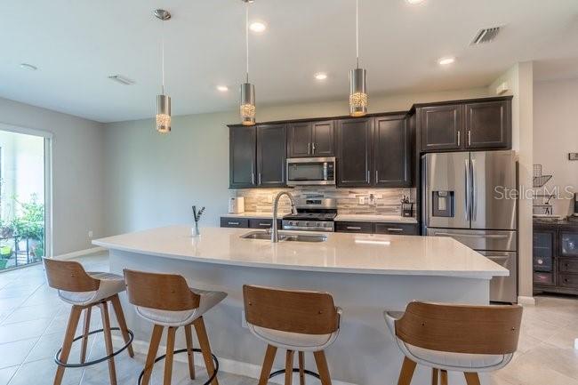 A modern kitchen features dark wood cabinets, a white quartz island, and four bar stools — 42982 PARKSIDE COURT, PUNTA GORDA, FL