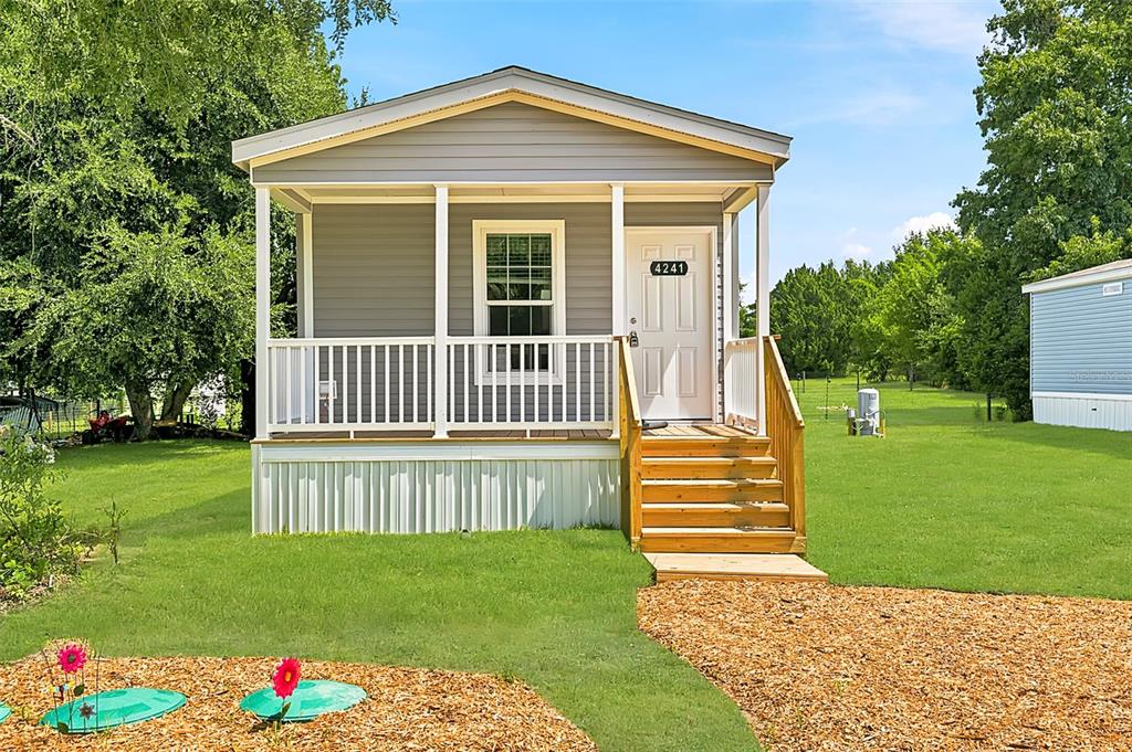 A small, gray-sided mobile home features a front porch with white railings and wooden stairs — 4241 E HAWAII LANE, HERNANDO, FL
