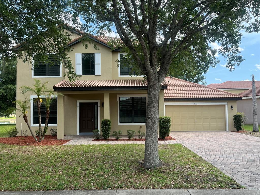 A two-story tan stucco house with a tile roof, a garage, and a front tree — 2821 SCENIC LANE, KISSIMMEE, FL