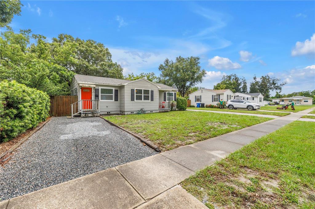 A single-story gray house with a bright orange front door and a gravel driveway — 416 61ST AVENUE NE, ST PETERSBURG, FL