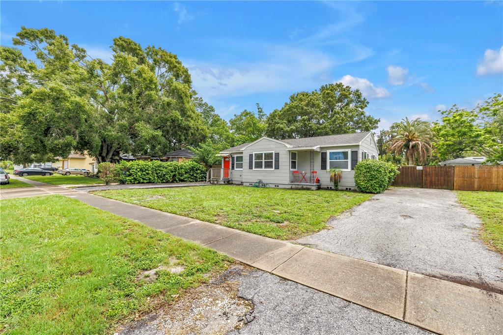 A single-story gray house with a front lawn, driveway, and large trees under a blue sky — 416 61ST AVENUE NE, ST PETERSBURG, FL