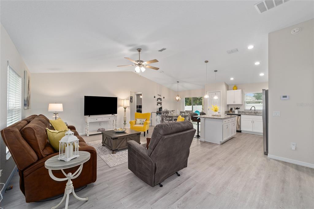 An open-concept living room and kitchen featuring light wood flooring and a vaulted ceiling — 4475 SW 149TH STREET, OCALA, FL