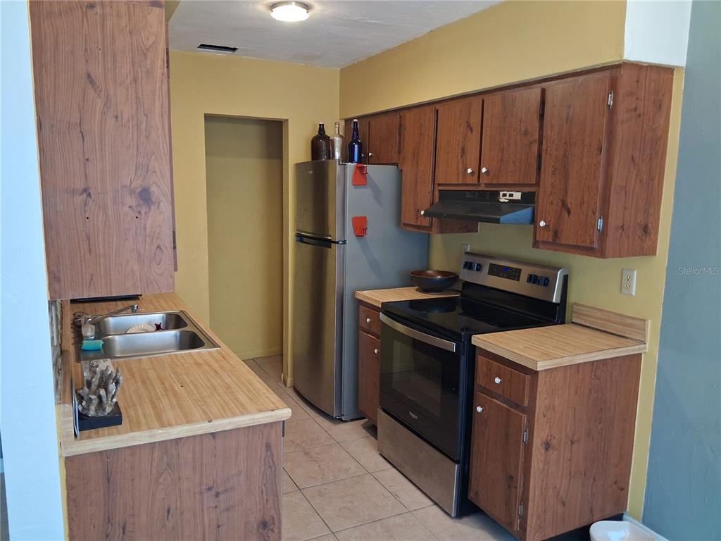 A kitchen features wood-grain cabinets, laminate countertops, stainless steel appliances, and yellow walls — 1977 SW 69TH DRIVE, GAINESVILLE, FL