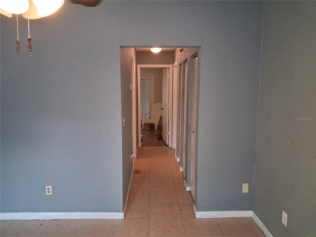 A hallway with tiled flooring leads from a gray-walled room toward a distant white chair — 1977 SW 69TH DRIVE, GAINESVILLE, FL