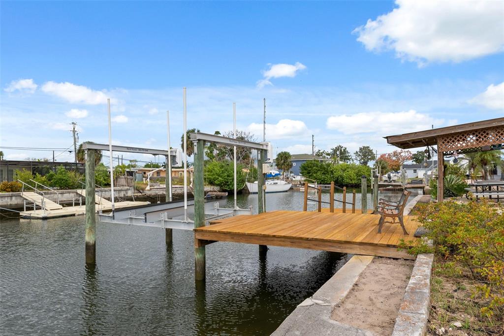 A wooden dock with a boat lift sits along a canal next to a seawall — 6719 ALBATROSS LANE, HUDSON, FL