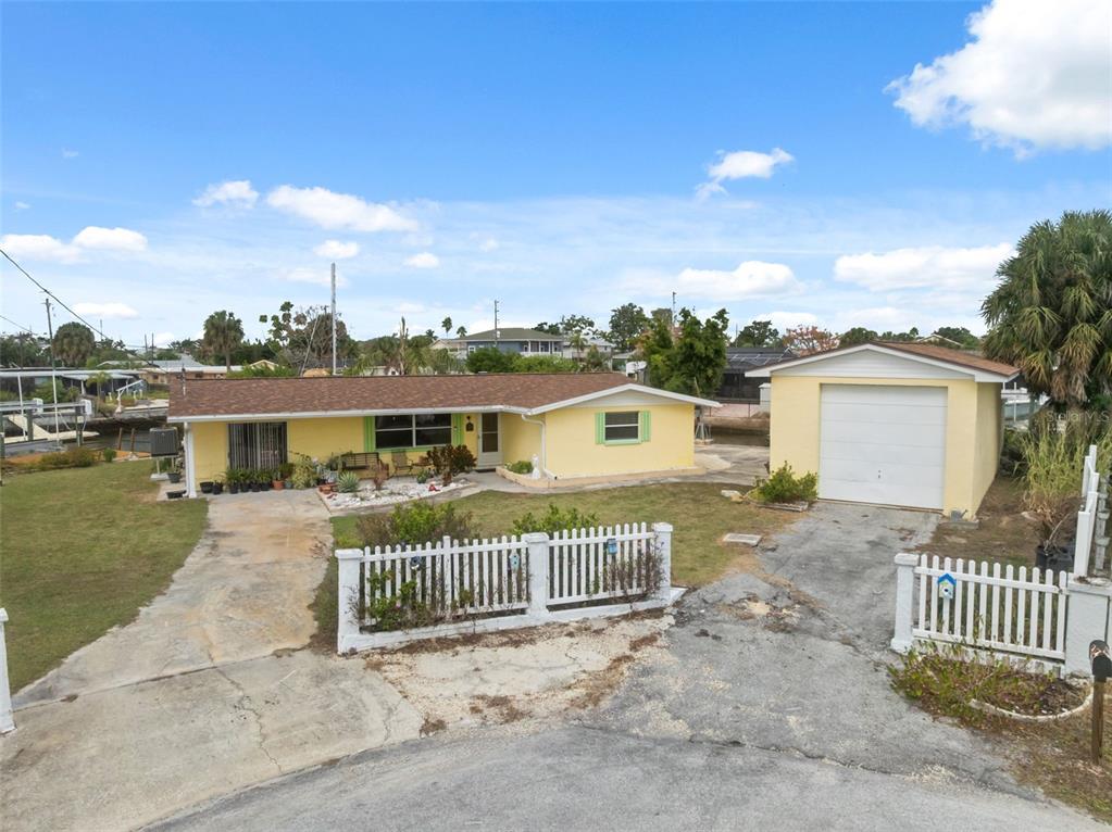 A yellow single-story house with a detached garage and white picket fence — 6719 ALBATROSS LANE, HUDSON, FL