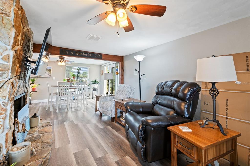 A living room with a stone fireplace, wood-look flooring, and a dining area beyond — 6719 ALBATROSS LANE, HUDSON, FL