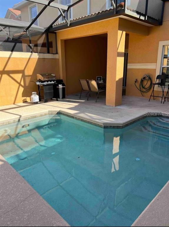 A swimming pool sits on a patio next to a covered outdoor dining area and grill — 8947 CANDY PALM RD, KISSIMMEE, FL