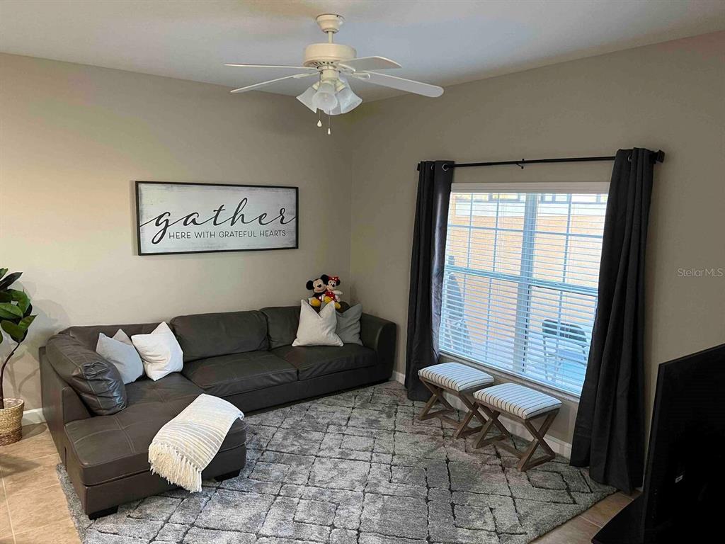 A living room features a dark leather sectional, a gray area rug, and a ceiling fan — 8947 CANDY PALM RD, KISSIMMEE, FL