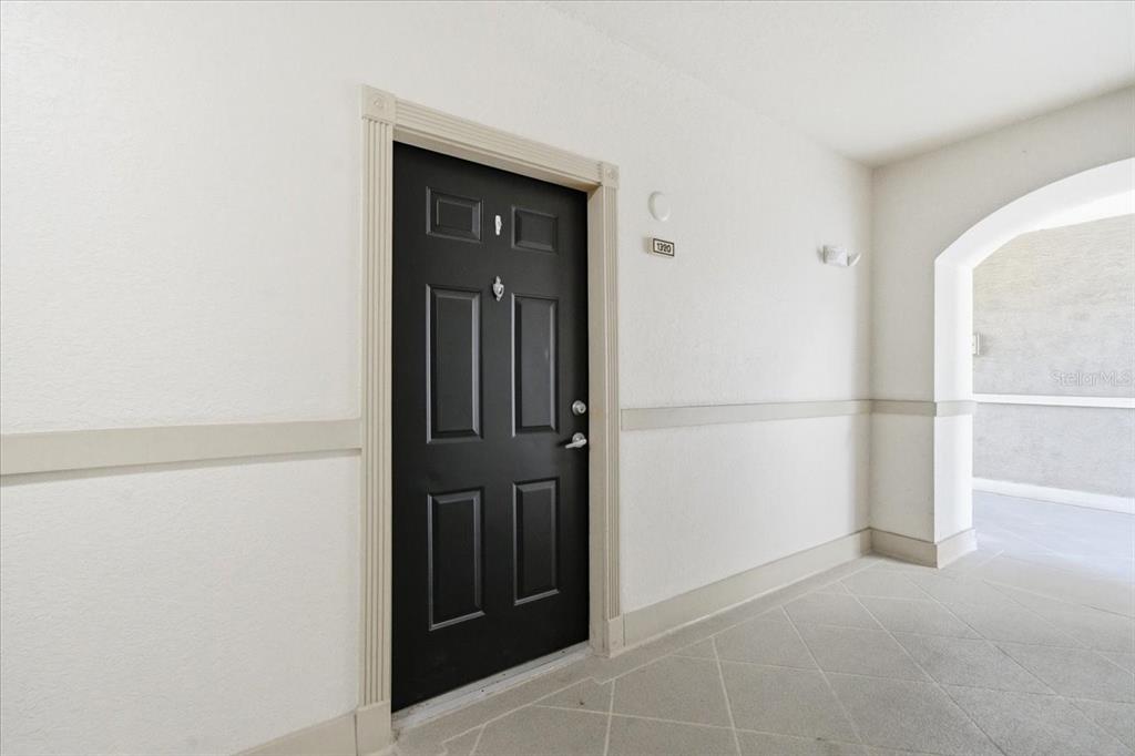 A black front door with a silver handle is set in a white hallway — 501 KNIGHTS RUN AVENUE UNIT 1320, TAMPA, FL