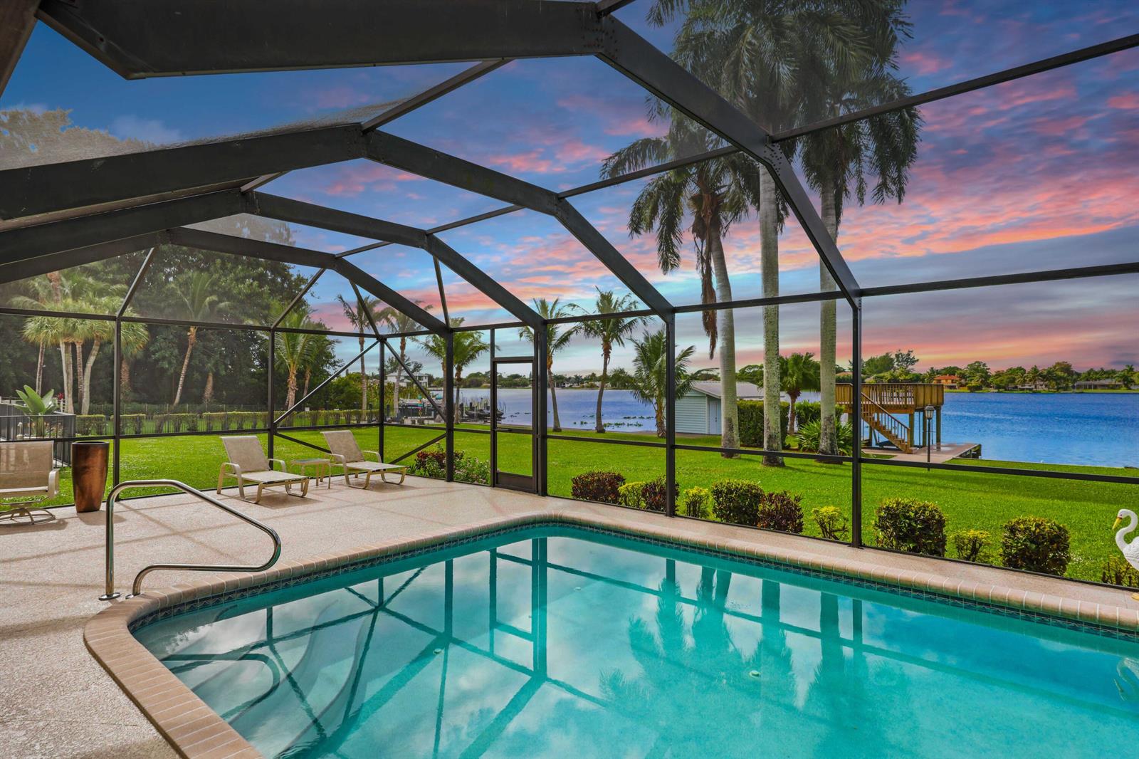 A screened-in pool patio overlooks a grassy lawn and a lake at sunset — 2097 Circle Place Drive, Lake Worth FL 33462, LAKE WORTH, FL