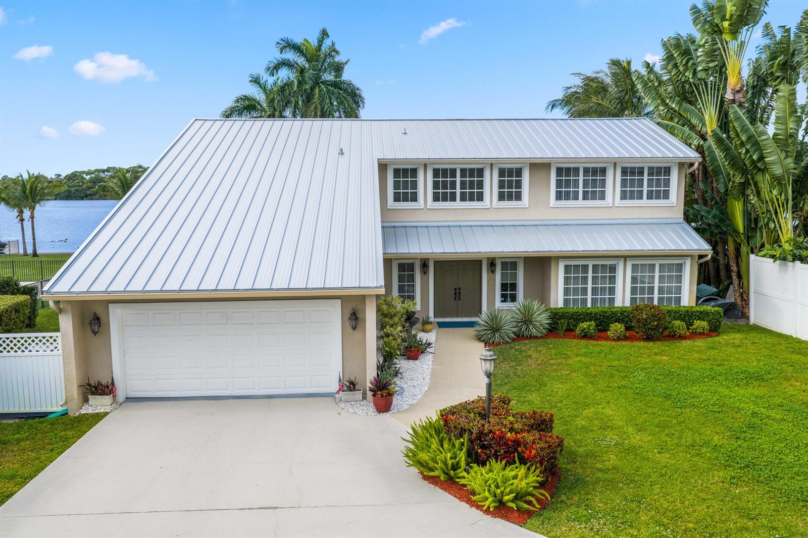 A two-story house with a metal roof, attached garage, and front lawn faces a lake — 2097 Circle Place Drive, Lake Worth FL 33462, LAKE WORTH, FL
