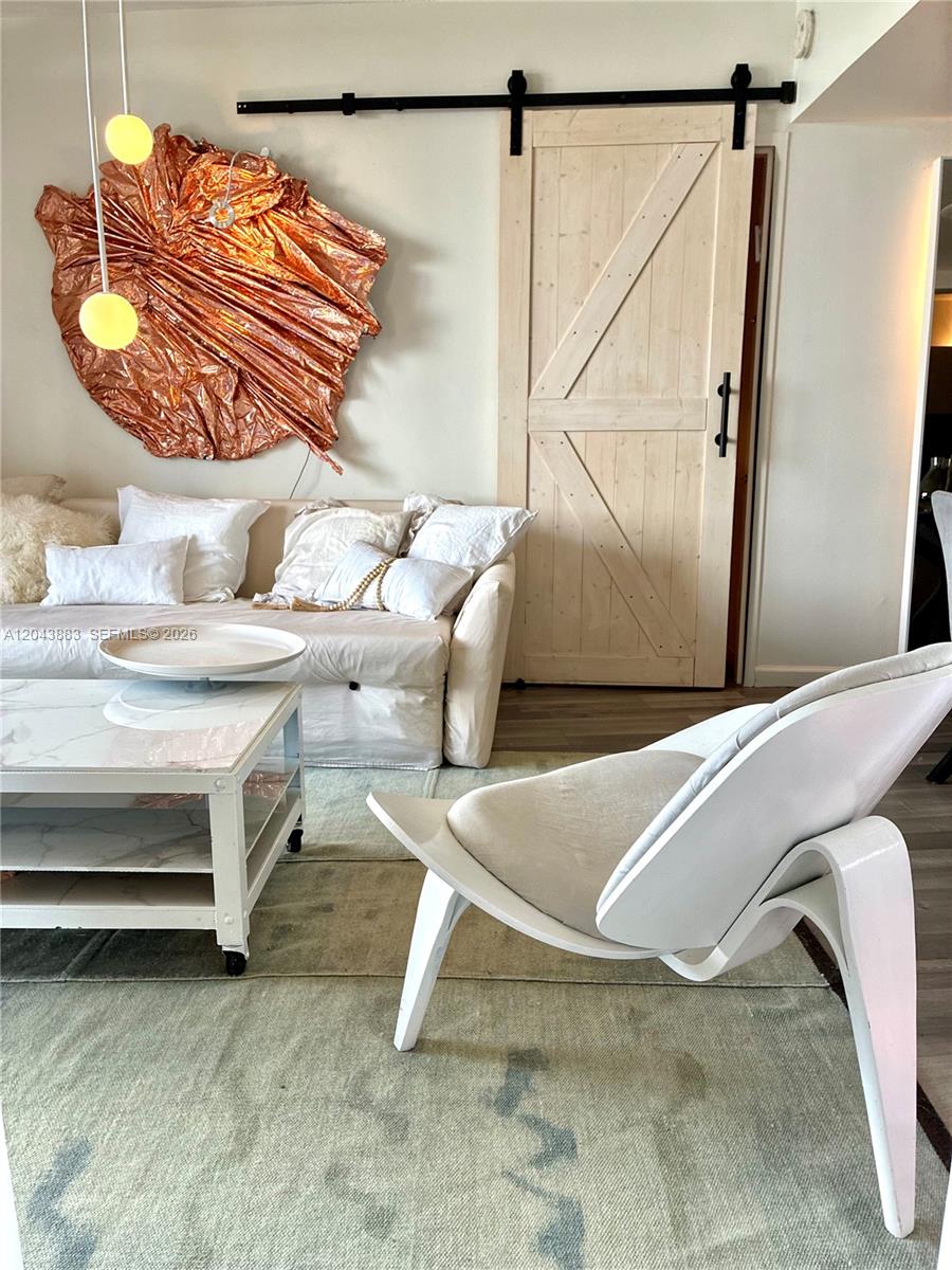A living room features a white sofa, a modern accent chair, and a sliding barn door — 900 Bay Dr # 207, Miami Beach FL 33141, MIAMI BEACH, FL