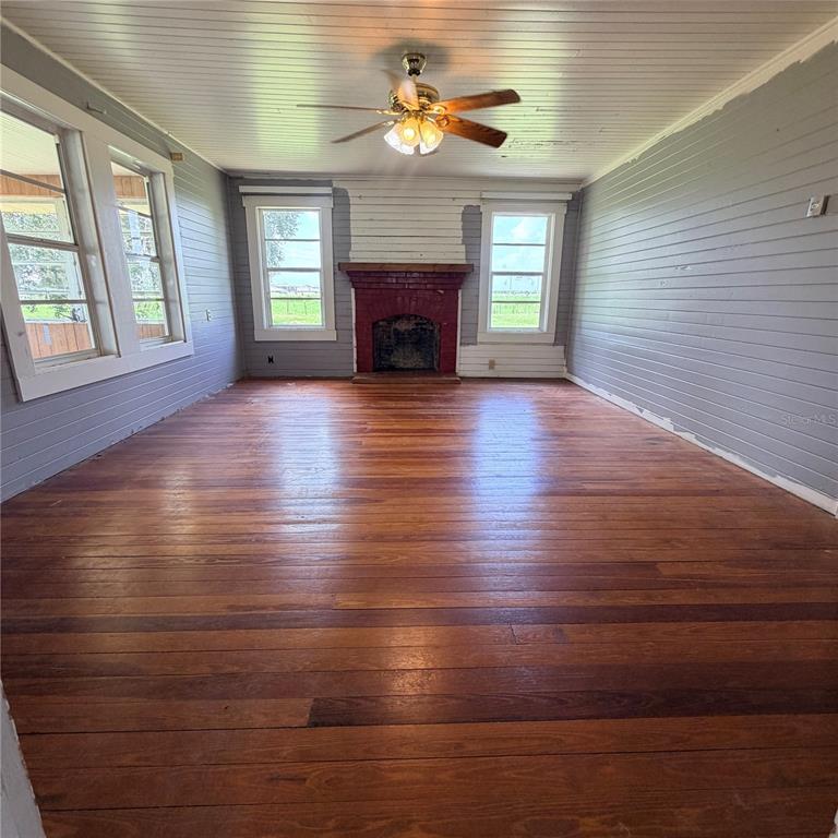 A living room features hardwood floors, a red brick fireplace, and gray horizontal wood walls — 15016 SCANT STREET, WIMAUMA, FL