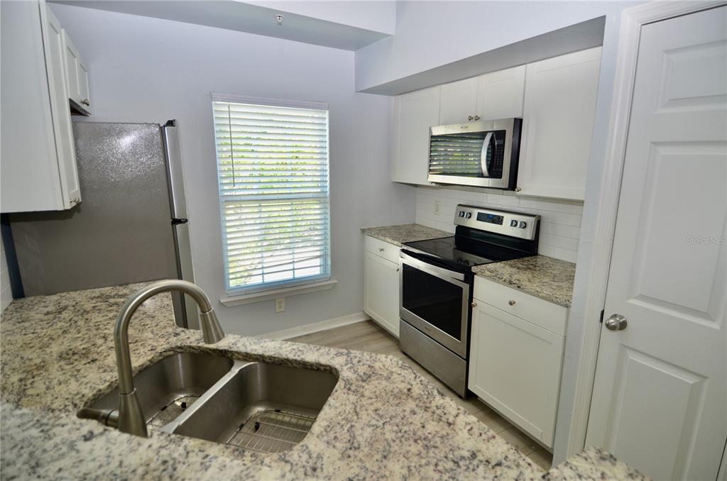 A kitchen features white cabinets, granite countertops, stainless steel appliances, and a double-basin sink — 5621 BIDWELL PARKWAY UNIT 202, SARASOTA, FL