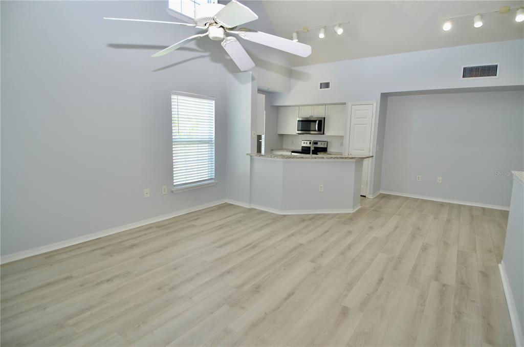 An open-concept living area features light wood-look flooring, a vaulted ceiling, and a kitchen pass-through — 5621 BIDWELL PARKWAY UNIT 202, SARASOTA, FL