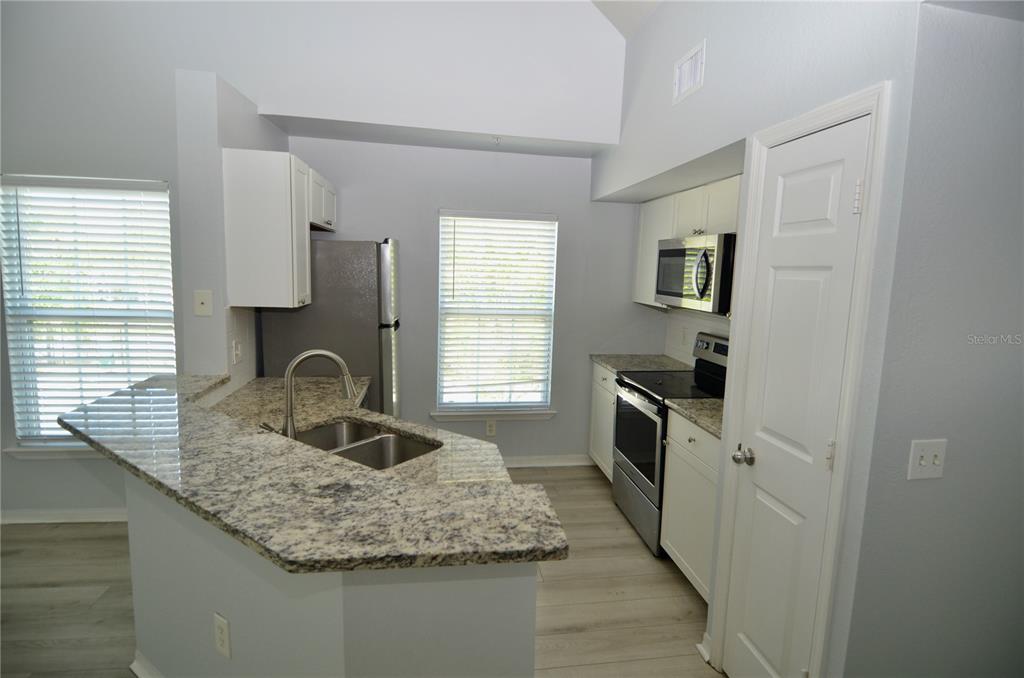 A kitchen features granite countertops, stainless steel appliances, white cabinetry, and light wood-look flooring — 5621 BIDWELL PARKWAY UNIT 202, SARASOTA, FL