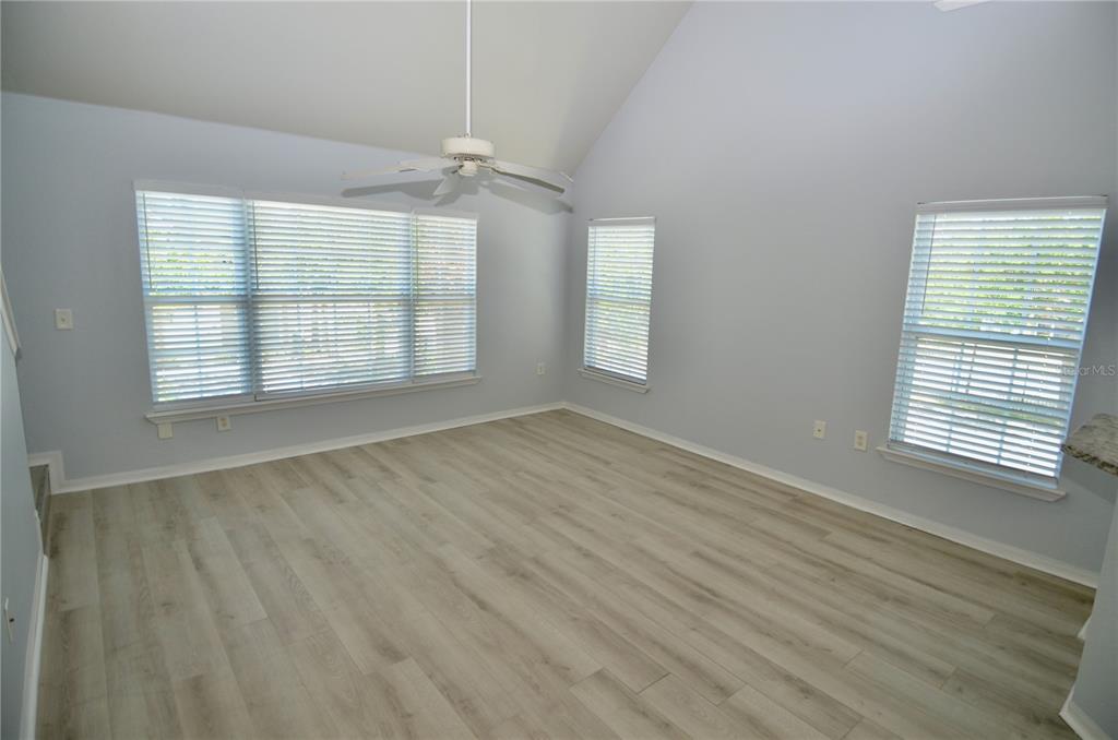 An empty room with light gray walls, wood-look flooring, a vaulted ceiling, and three windows — 5621 BIDWELL PARKWAY UNIT 202, SARASOTA, FL