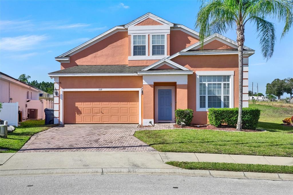 A two-story peach-colored house features a two-car garage, a blue front door, and a palm tree — 359 VIZCAY WAY, DAVENPORT, FL