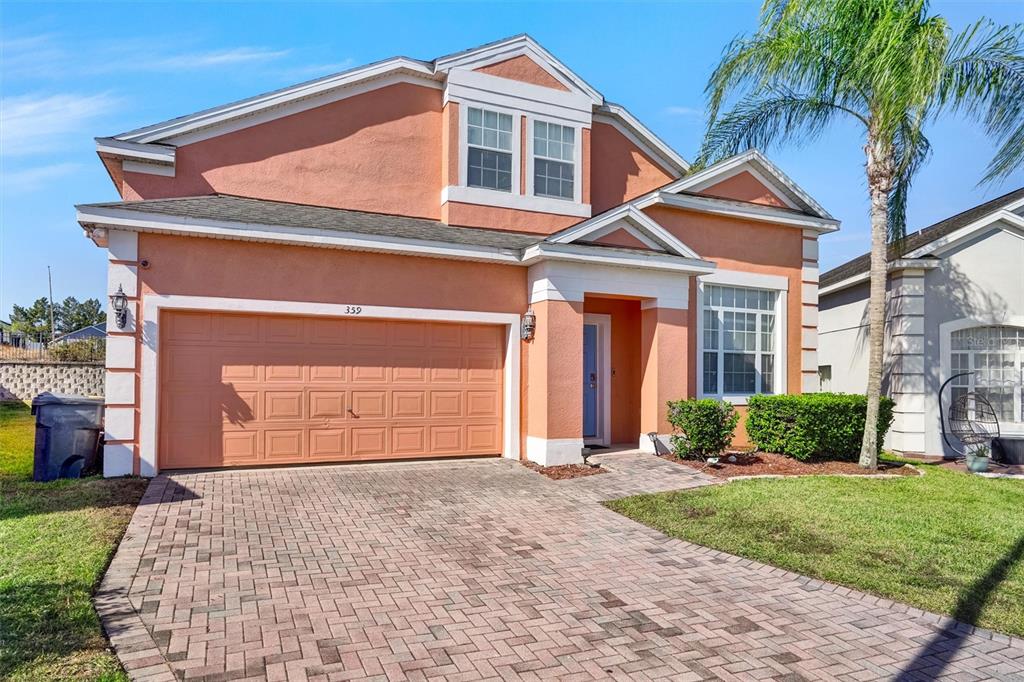 A two-story peach-colored house features a paved driveway, a two-car garage, and a palm tree — 359 VIZCAY WAY, DAVENPORT, FL