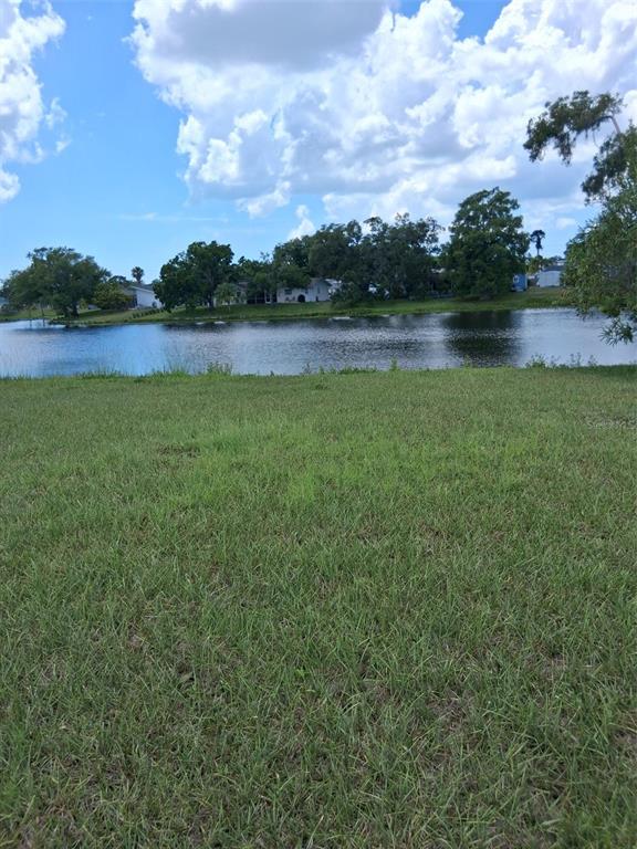 A grassy lawn leads to a pond with trees and houses in the background — 6614 SABINA ROAD, SARASOTA, FL