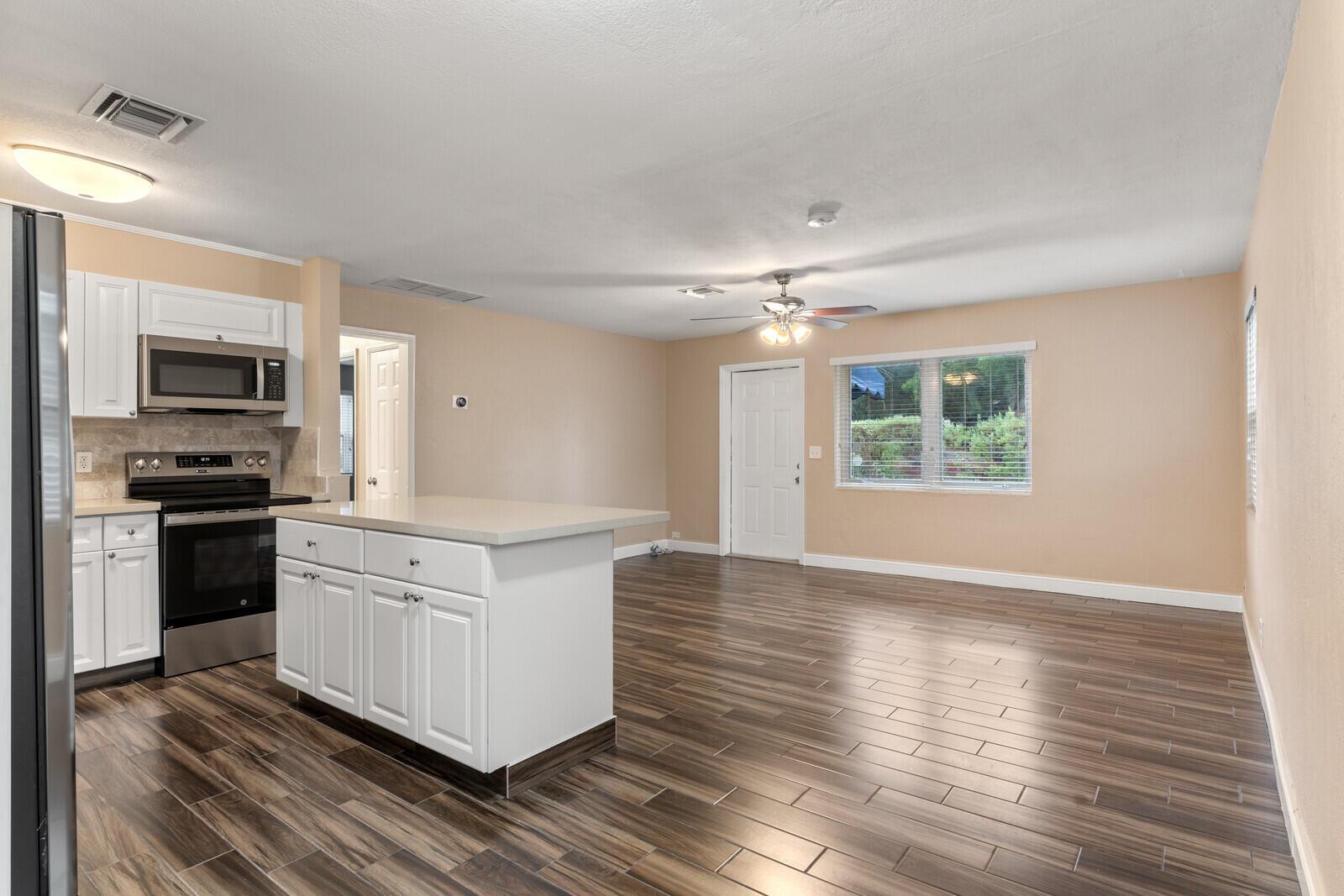 A kitchen with white cabinets and an island opens into a living area with wood-look flooring — 957 30th Street, West Palm Beach FL 33407, WEST PALM BEACH, FL